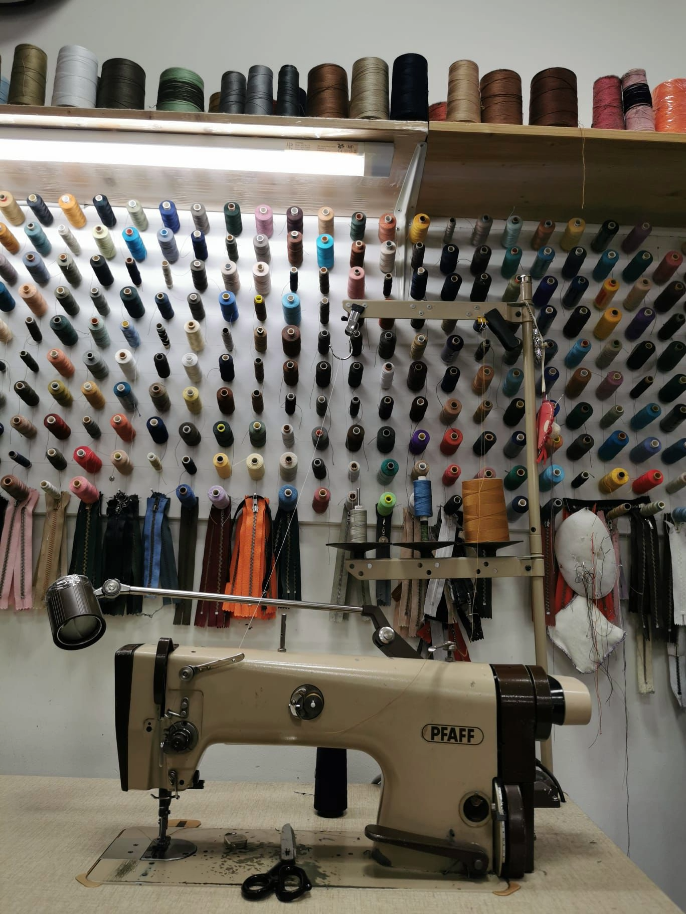 Pfaff Industrienähmaschine vor Wand mit hunderten Garnrollen in allen Farben